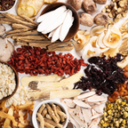 An overhead flat-lay arrangement of various dried and fresh herbal ingredients arranged around a white central background.