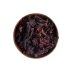Dried dark red and purple hibiscus flowers piled in a round brown ceramic bowl, photographed from above on a plain white background.
