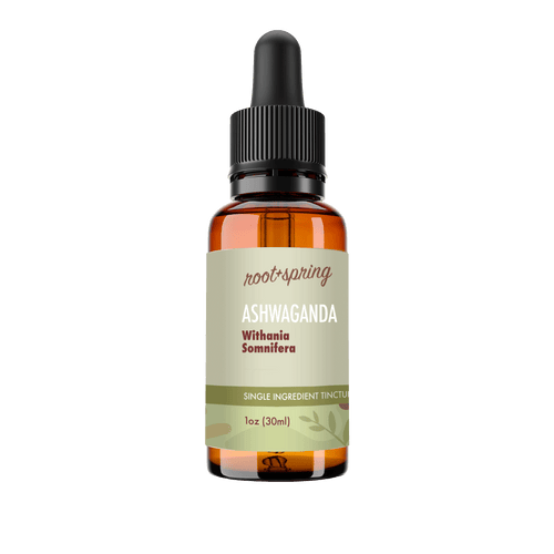 A 1 oz amber glass dropper bottle of Root+Spring Ashwaganda tincture with a black dropper cap and a light olive-green label, shown on a transparent background.